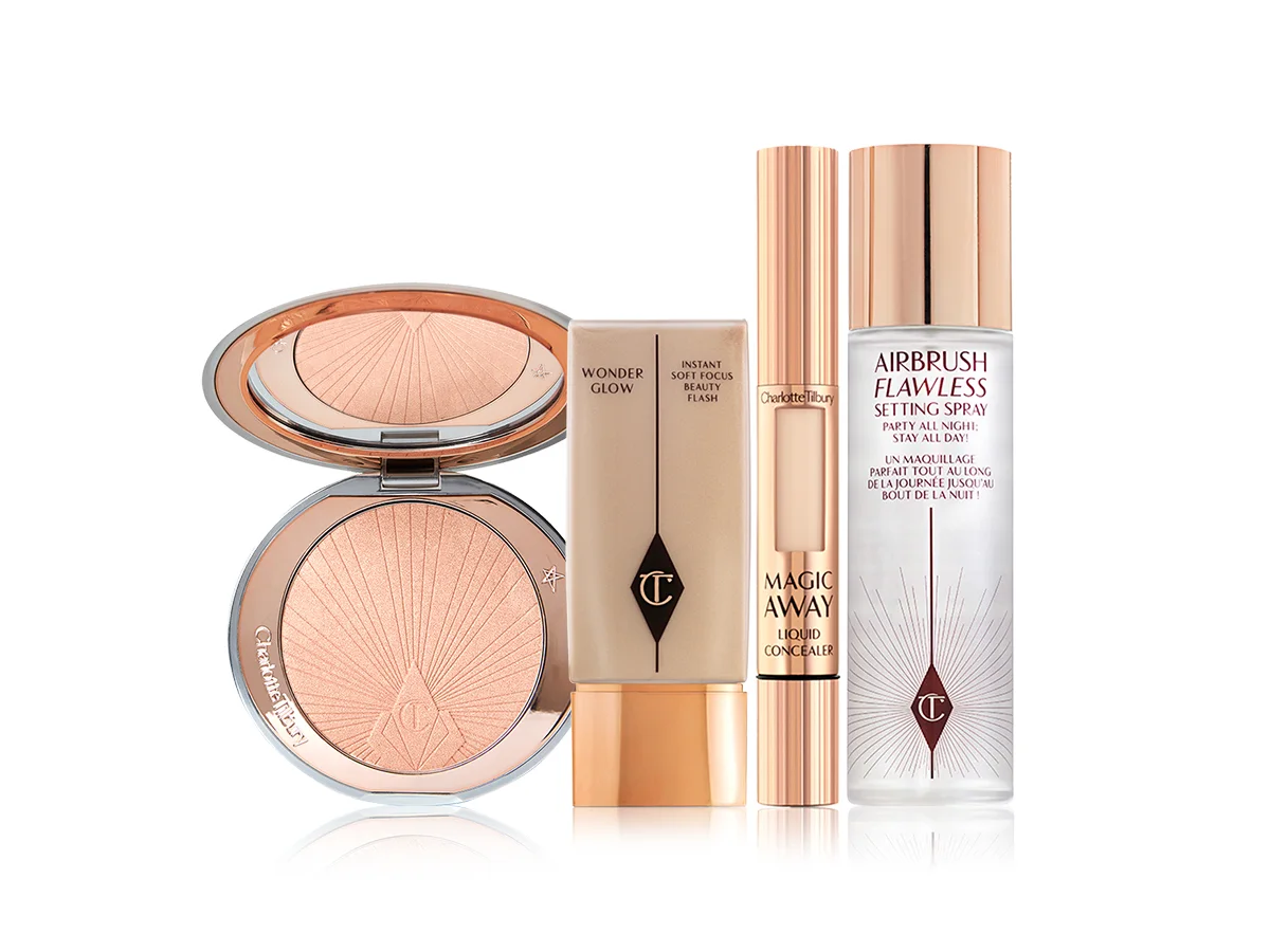 Bronzer compact with a mirrored-lid in a light shade, primer in a glowy primer in a clear bottle with gold-coloured lid, concealer in gold packaging, and setting spray. 
